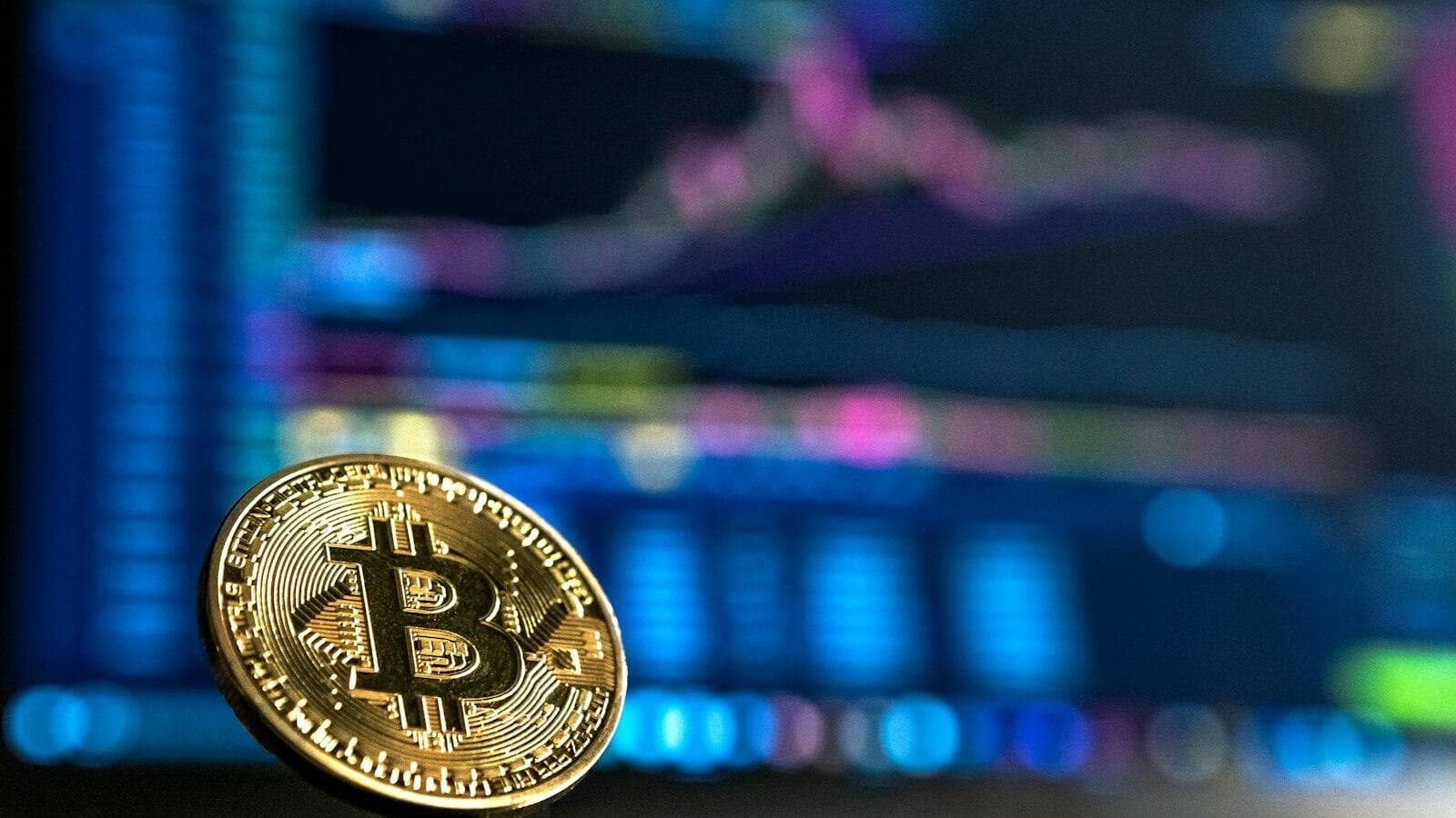 A Bitcoin coin in front of a screen of price charts