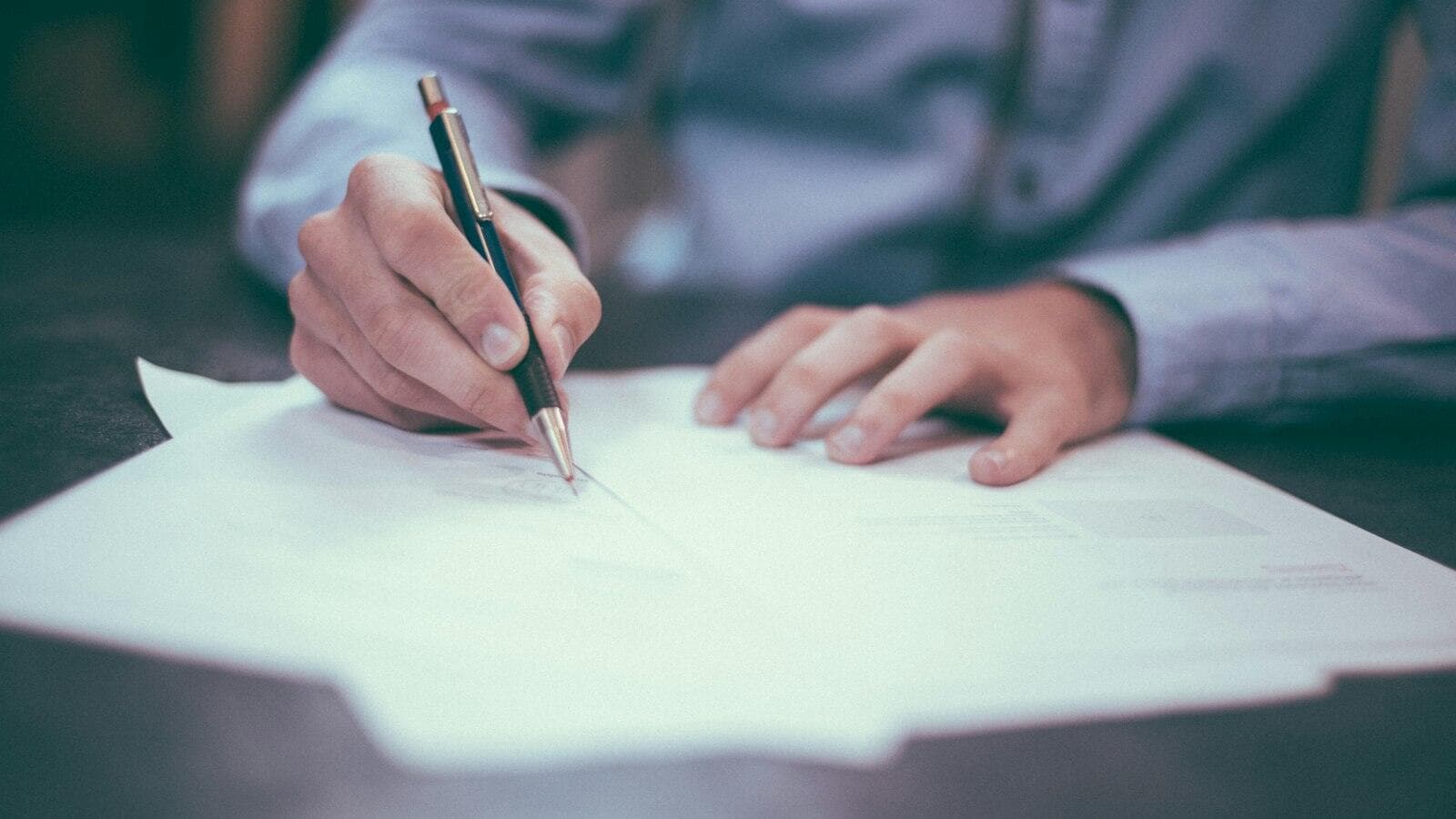 Hands filling in a paper form with a pen